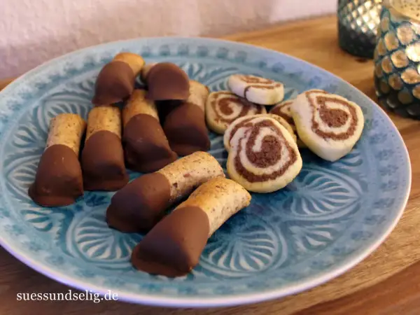 Mandelstangen mit Marzipan und schokoladenüberzogenen Keksen auf blauem Teller.