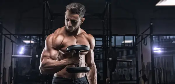 Uomo muscoloso in palestra con manubrio, focus sulla definizione muscolare, integrando la creatina per massimizzare i risultati.