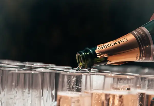 Versando champagne da una bottiglia in una fila di bicchieri, mostrando diversi tipi di champagne.