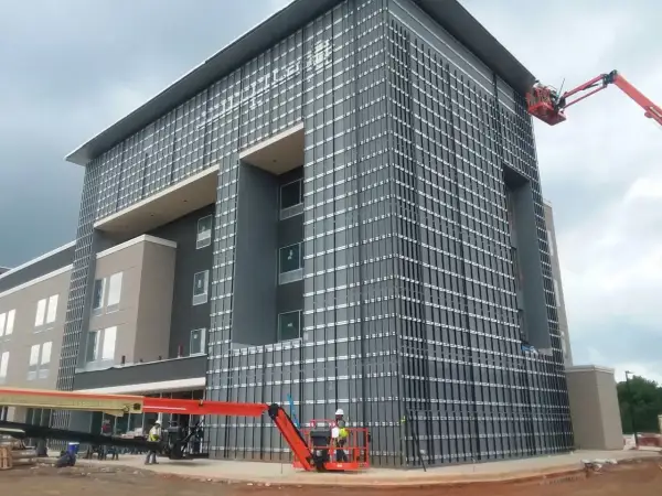 Instalación de sistemas de fachadas ventiladas en edificio moderno. Obreros en plataformas elevadoras trabajan en la colocación de paneles.