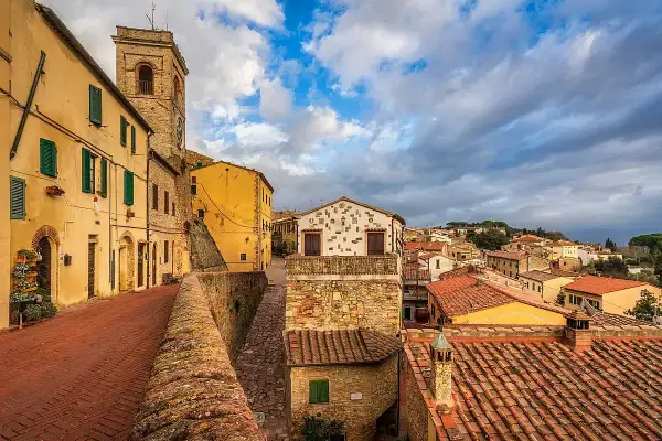 Un vicolo con case gialle e un campanile a Montescudaio. Tetti rossi e cielo nuvoloso, un'atmosfera suggestiva per scoprire cosa vedere.