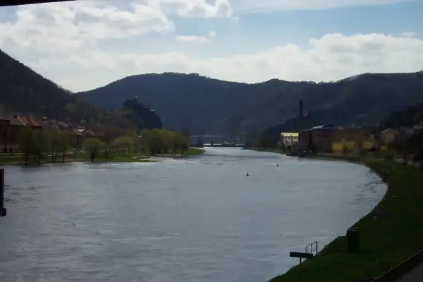 Flusslandschaft bei Ústí nad Labem mit bewaldeten Hügeln, Industriegebäuden und einer Stadt am Ufer.