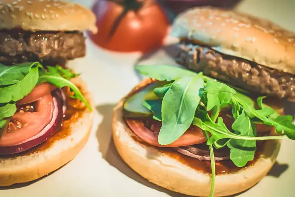 Dwa domowe hamburgery z bułką, kotletem, pomidorem, czerwoną cebulą i rukolą.