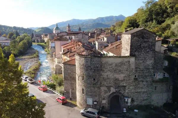 Antica porta in pietra lungo la via del Volto Santo, con fiume e case arroccate sui monti.