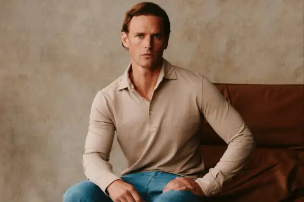Ein Mann sitzt lässig in einem beigen Langarm-Polohemd, das an italienische Poloshirts für Herren erinnert.