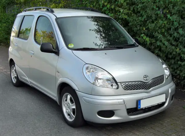 Srebrny Toyota Yaris Verso zaparkowany przy żywopłocie.