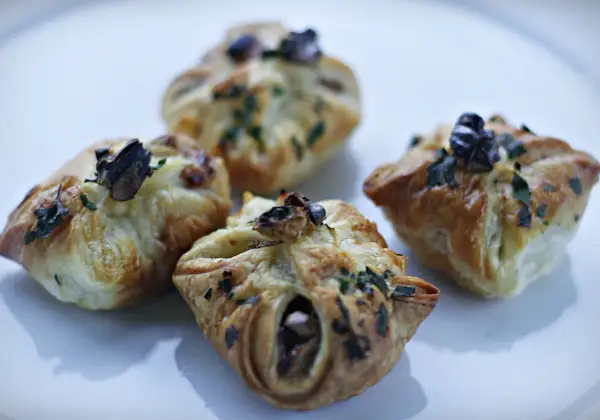 Cztery apetyczne paczuszki z ciasta francuskiego z gruszkami i gorgonzolą, posypane ziołami.