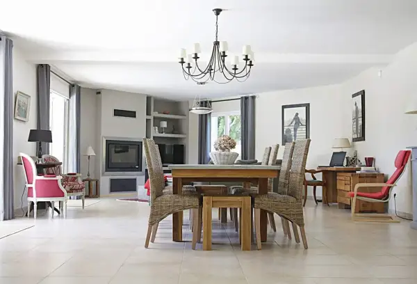 Elegancki, czarny żyrandol do salonu nad stołem z wiklinowymi krzesłami. W tle kominek i wygodne fotele.