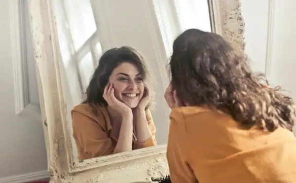 Donna sorride guardandosi allo specchio, un momento di riflessione sull'effetto specchio psicologia e sull'accettazione di sé.