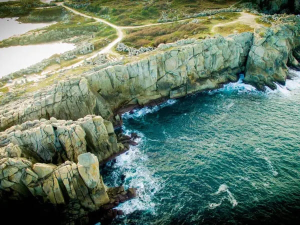 Impresionantes acantilados galicia, con el mar azul turquesa rompiendo contra las rocas. Senderos serpentean por la vegetación verde.