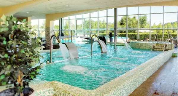 Piscina interior con cascadas de agua y vistas al exterior, ideal para una experiencia de spa relajante.