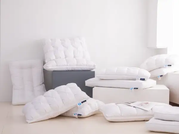 A pile of fluffy white down pillows, some with tufted patterns. One new down pillow smells bad, but the others look inviting.