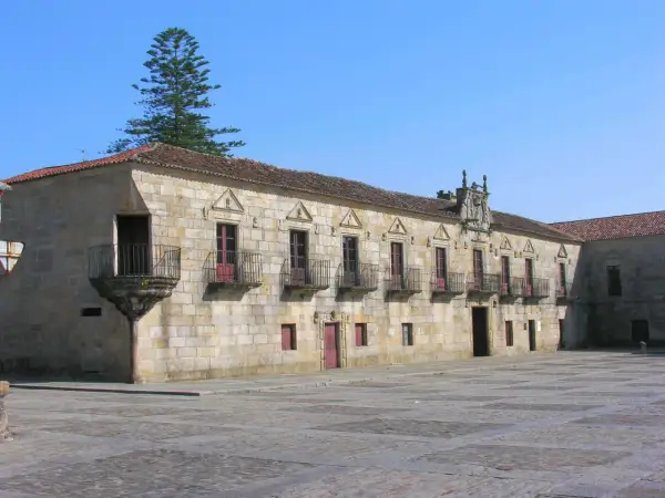 El Pazo de Fefiñanes, un edificio de piedra con balcones de hierro forjado, se alza bajo un cielo azul.