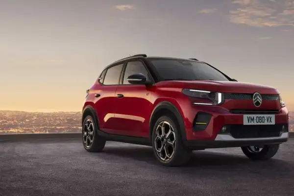 Nowy, czerwony Citroen C3 2025 z czarnym dachem i felgami, zaparkowany na tle miasta o zachodzie słońca.