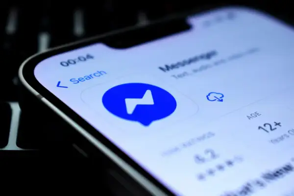 Ikona aplikacji Messenger na ekranie telefonu. Widoczne dymki czatu, wyszukiwarka i informacja o wieku 12+.