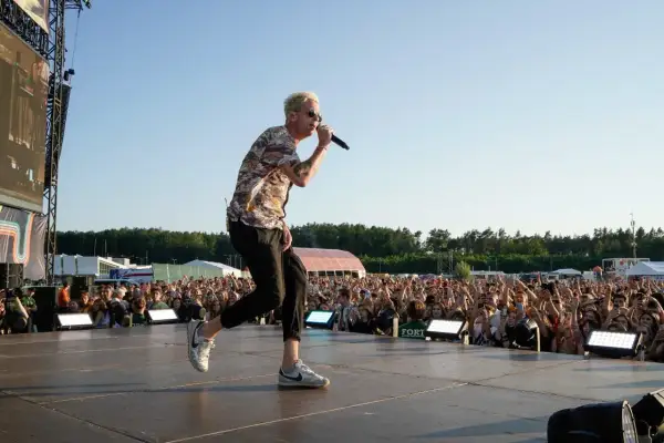 Wokalista One Republic na koncercie, śpiewa do mikrofonu na scenie przed rozentuzjazmowanym tłumem fanów.