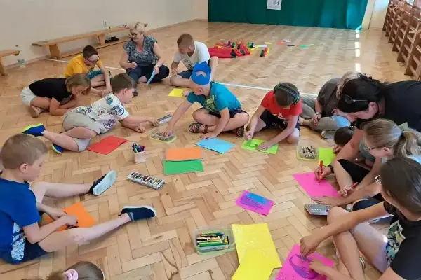 Dzieci klas 1-3 biorą udział w zabawach integracyjnych, rysując i kolorując na podłodze.