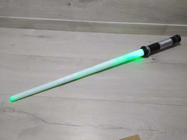 Zielony miecz Star Wars leży na drewnianej podłodze.
