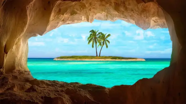 Vista da una grotta su un'isola con palme e un mare cristallino, il mare più bello del mondo.