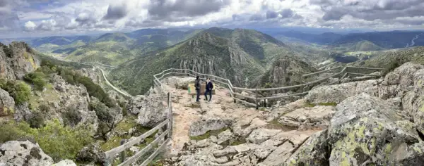 Dos personas admiran el paisaje montañoso desde el mirador del Cerro del Viso. El cielo está nublado.