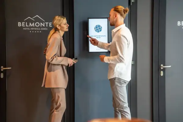 Elegancko ubrana para dyskutuje przy ekranie informacyjnym w hotelu Belmonte.