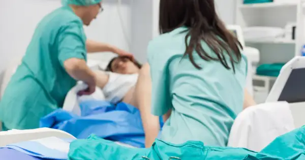 Personel medyczny zajmuje się pacjentką po porodzie. Widoczne są zielone fartuchy i sprzęt medyczny.
