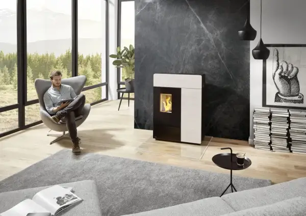 Un homme lit dans un fauteuil près d'un poêle moderne. Le **carrelage derrière le poêle** en marbre noir crée un contraste saisissant.