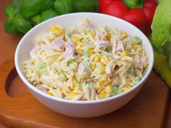 Pyszna sałatka z makaronem orzo, kukurydzą, szynką i selerem, polana kremowym sosem.