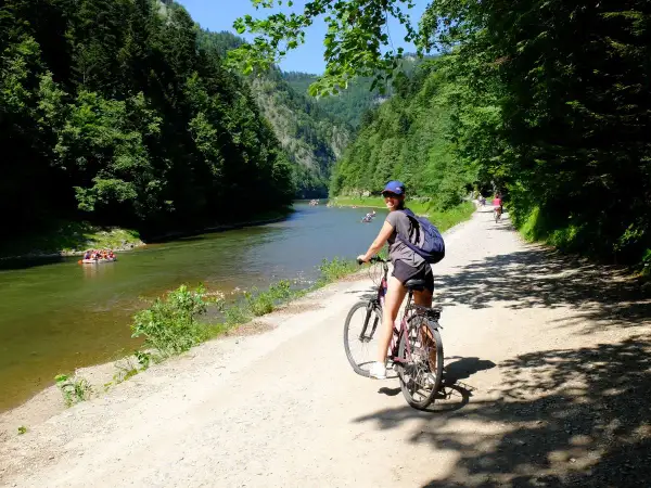 Dziewczyna na rowerze na malowniczej trasie rowerowej w Szczawnicy. W tle Dunajec z tratwami i zalesione góry.