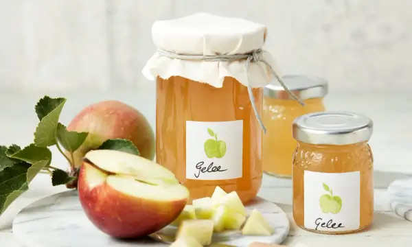 Zwei Gläser mit selbstgemachtem Apfelgelee, daneben frische Äpfel und gewürfelte Apfelstücke. Ein leckeres Apfelgelee Rezept zum Nachmachen.