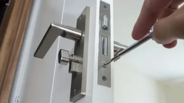 Réparation d'une poignée de porte qui claque avec le vent. Un tournevis ajuste la serrure.