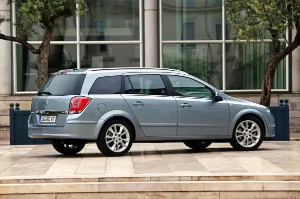 Srebrny Opel Astra H kombi stoi przed nowoczesnym budynkiem.