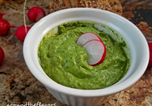 Zielone pesto z liści rzodkiewki w białej miseczce, ozdobione plasterkami rzodkiewki.