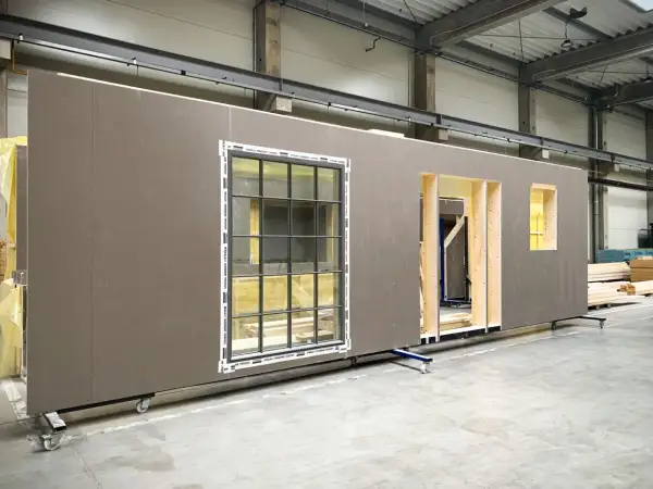 Gotowe ściany drewniane prefabrykowane z oknami i otworami na drzwi, czekające na montaż.