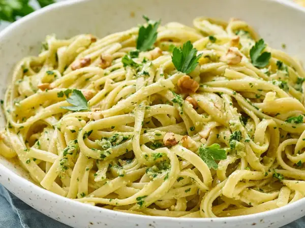 Pasta con pesto cremosa, adornada con nueces y perejil fresco. Un plato italiano delicioso y vibrante.