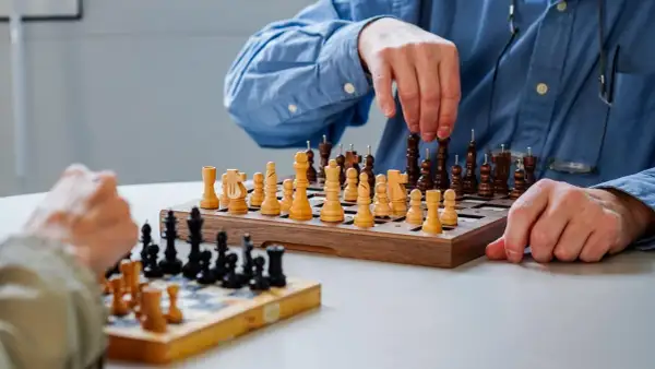 Deux personnes jouent aux échecs. Les pièces ont des ergots pour aider à les identifier, rendant ce jeu accessible aux aveugles.