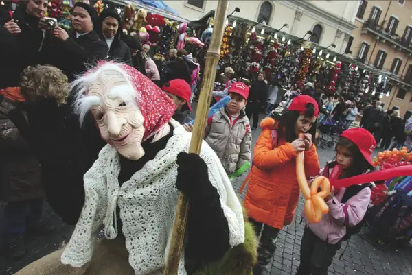 Una maschera della Befana saluta la folla, mentre i bambini giocano con palloncini gonfiabili. Si festeggia la Befana!