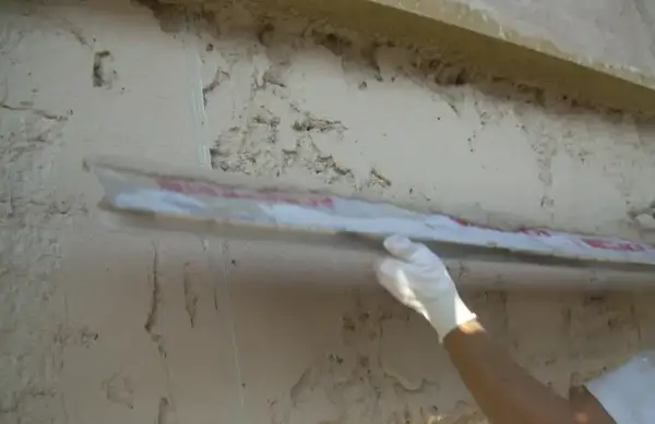 Applicazione di intonaco traspirante su una parete grezza con una spatola. La finitura garantisce la salute dell'edificio.