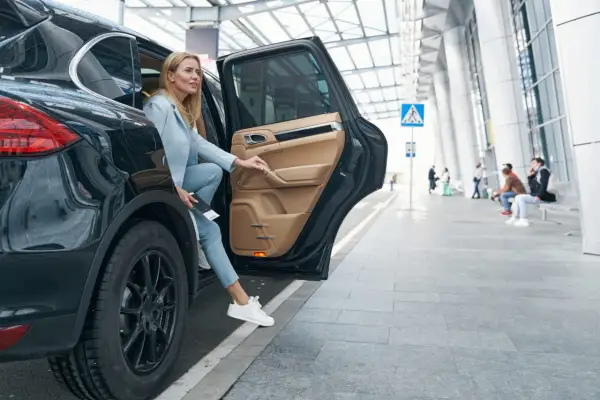 Kobieta wysiada z luksusowego SUV-a, trzymając dokumenty, które mogą być związane z umową użyczenia samochodu.