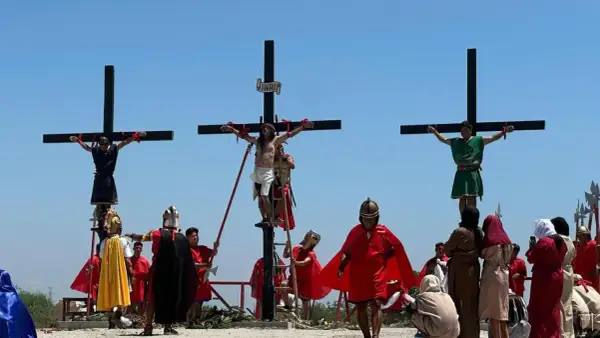 Nachstellung, wie Jesus stirbt am Kreuz, mit zwei weiteren Männern, die ebenfalls gekreuzigt werden. Soldaten in römischer Kleidung und Zuschauer sind anwesend.