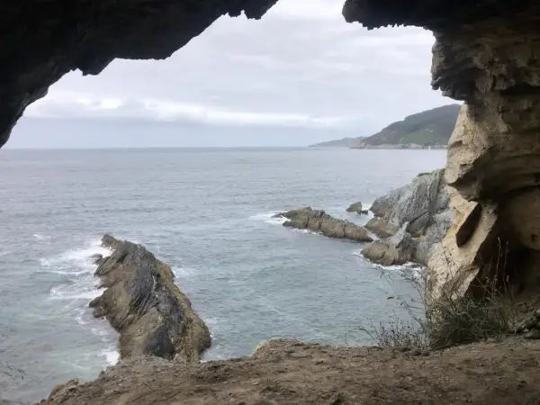 Vista desde la cova da doncela. El mar agitado choca contra las rocas mientras una vela solitaria navega en el horizonte.