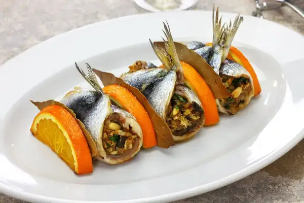 Sarde a beccafico su un piatto bianco, guarnite con fette d'arancia e foglie di alloro. Un piatto tradizionale siciliano.