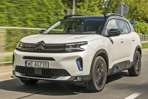 Biały Citroen C5 Aircross 2025 z czarnym dachem pędzi po drodze, otoczony zielenią.