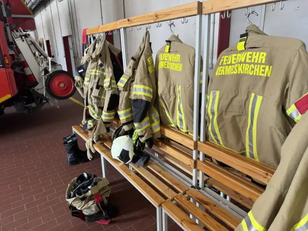 Schutzkleidung für die ehrenamtliche Feuerwehr hängt bereit. Stiefel und Helme liegen auf der Bank.