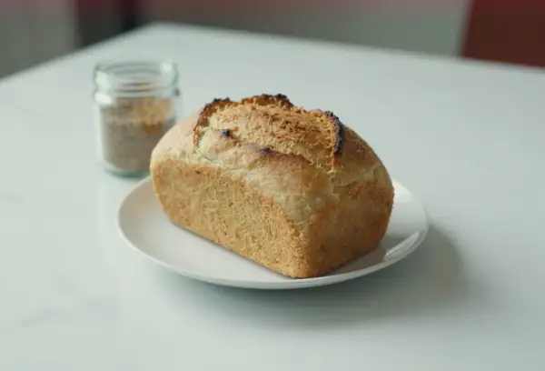 Chleb z mąki ryżowej, lekko przypieczony, na białym talerzyku. Obok słoiczek z ziarnami.