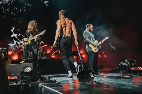 Imagine Dragons na koncercie w Polsce: wokalista bez koszulki, gitarzyści grający na scenie.