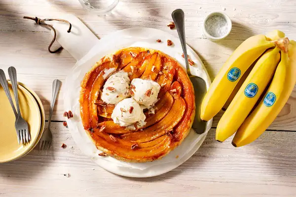 Eine köstliche gebackene Banane Tarte mit Vanilleeis und Pekannüssen, daneben frische Chiquita Bananen.
