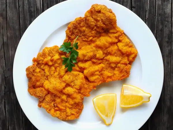 Ein knuspriges Wiener Schnitzel auf weißem Teller, garniert mit Petersilie und Zitronenspalten. Perfekt für einen herzhaften Genuss.