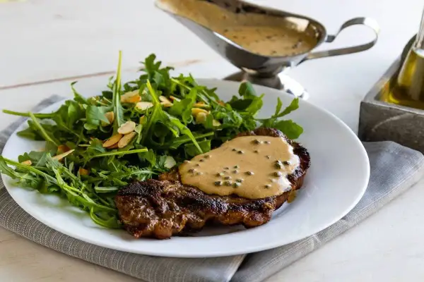 Un succulento filetto al pepe verde, nappato con salsa cremosa, servito con un'insalata fresca di rucola e mandorle.