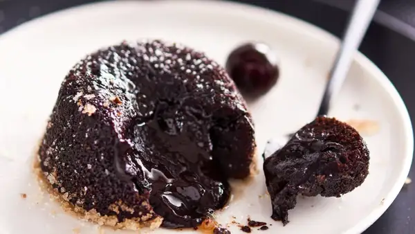 Tortino cuore caldo con cioccolato fuso che cola, perfetto per una ricetta infallibile. Un ciliegino completa il piatto.